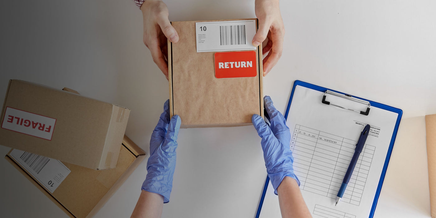 Person wearing gloves holding a box labeled 'RETURN' with a clipboard and pen on a table.
