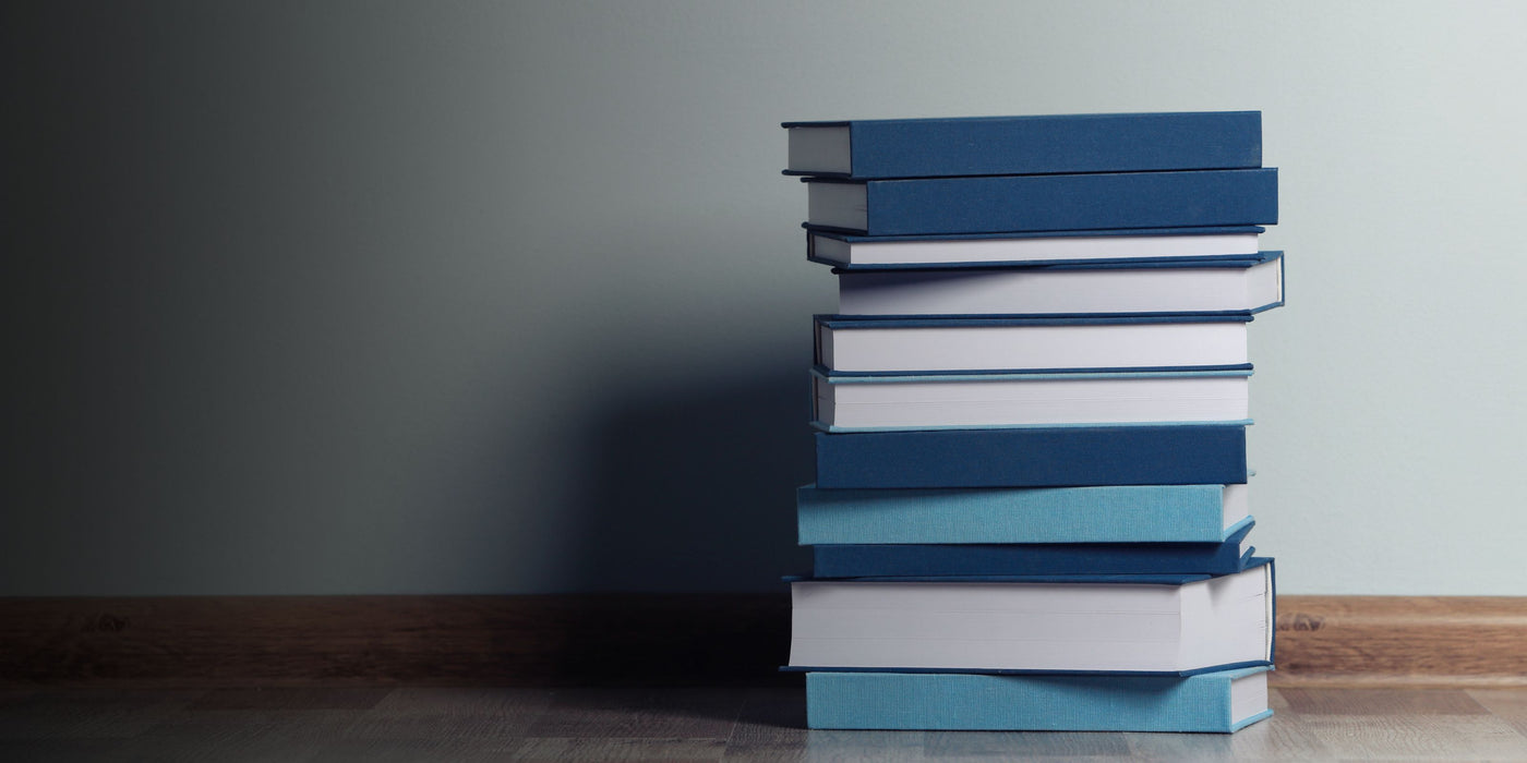 Stack of books with blue and white spines on a wooden surface against a gray wall.